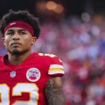 The individual in the photograph is Trent McDuffie, a cornerback who played for the Kansas City Chiefs from 2022 to early 2026. Image Details Alt Text: A close-up, high-resolution photograph of NFL cornerback Trent McDuffie wearing a red Kansas City Chiefs jersey with white and yellow accents