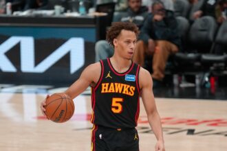 Dyson Daniels #5 of the Atlanta Hawks dribbles a basketball with his right hand while looking toward the basket. He is wearing the team's black Statement Edition uniform and bright blue sneakers.