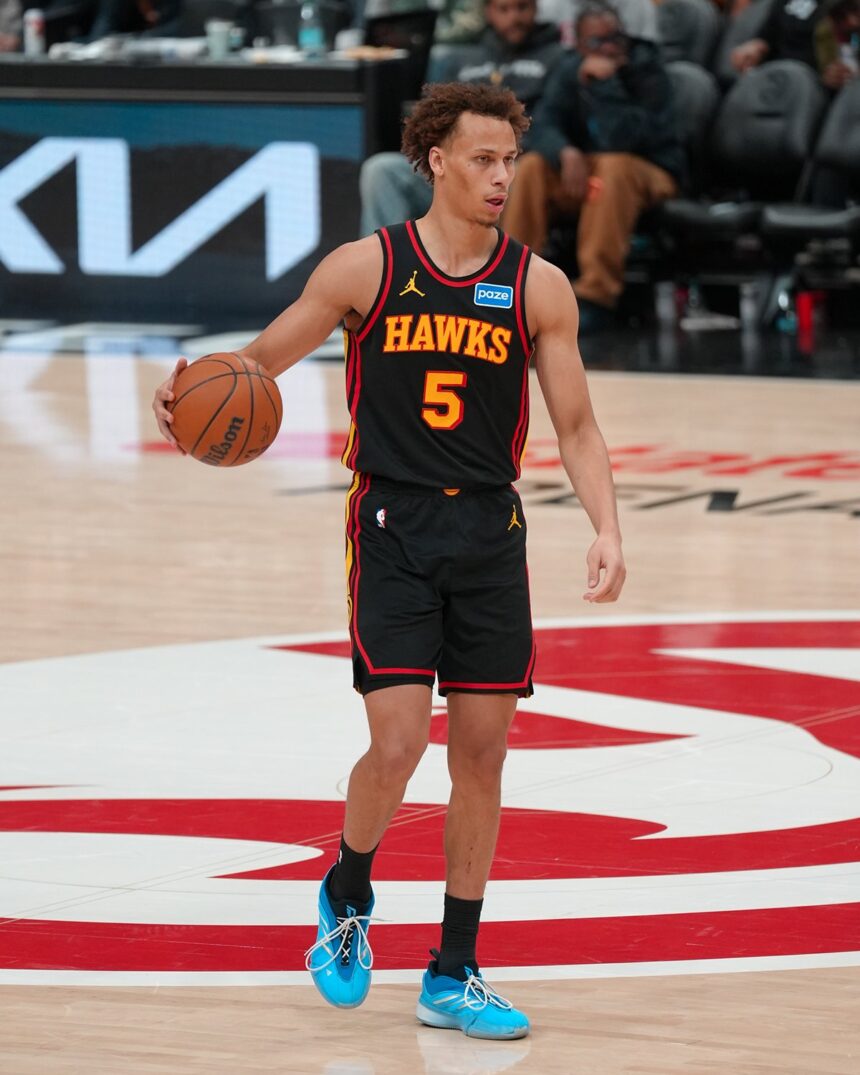 Dyson Daniels #5 of the Atlanta Hawks dribbles a basketball with his right hand while looking toward the basket. He is wearing the team's black Statement Edition uniform and bright blue sneakers.