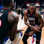 Justin Edwards #33 of the Philadelphia 76ers, showing a large tattoo on his left shoulder, grips a basketball and smiles while celebrating with a teammate whose back is to the camera.