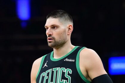 A medium shot of Boston Celtics center Nikola Vučević (wearing jersey number 4) looking off-camera with a serious expression. He is wearing a black Celtics "Statement Edition" jersey with green trim.