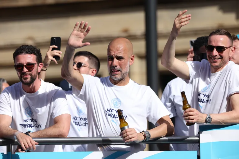 Manchester City manager Pep Guardiola, centre, takes part in an open-top bus parade in Manchester, England, on May 25. 2026
